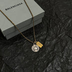 Gold chain necklace with round silver medallion and Cancer charm on black surface