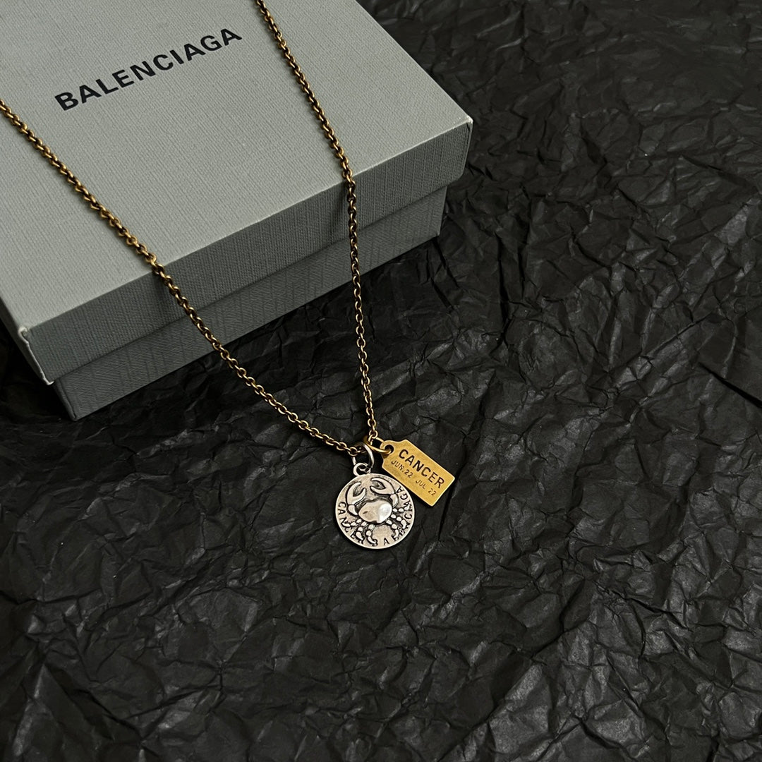 Gold chain necklace with round silver medallion and Cancer charm on black surface