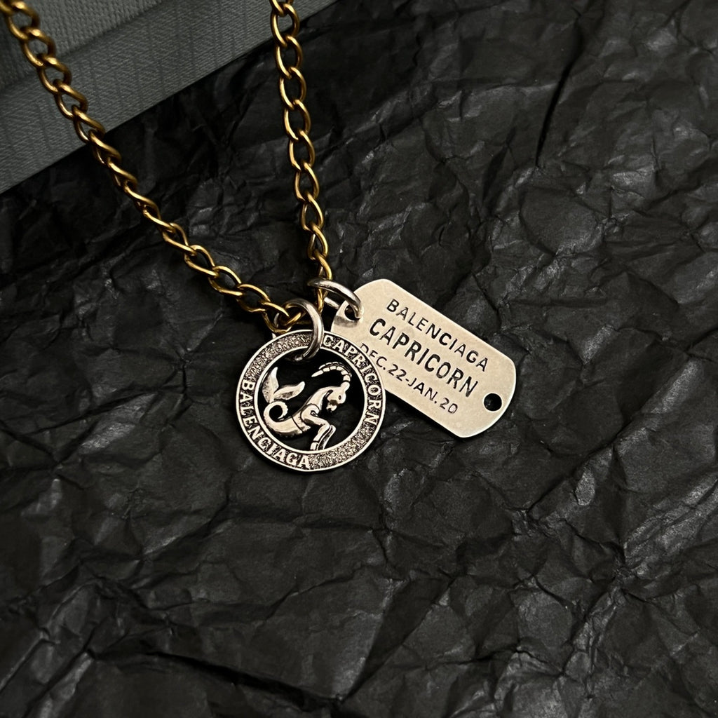 Gold charm necklace with circular zodiac coin and beige engraved name tag