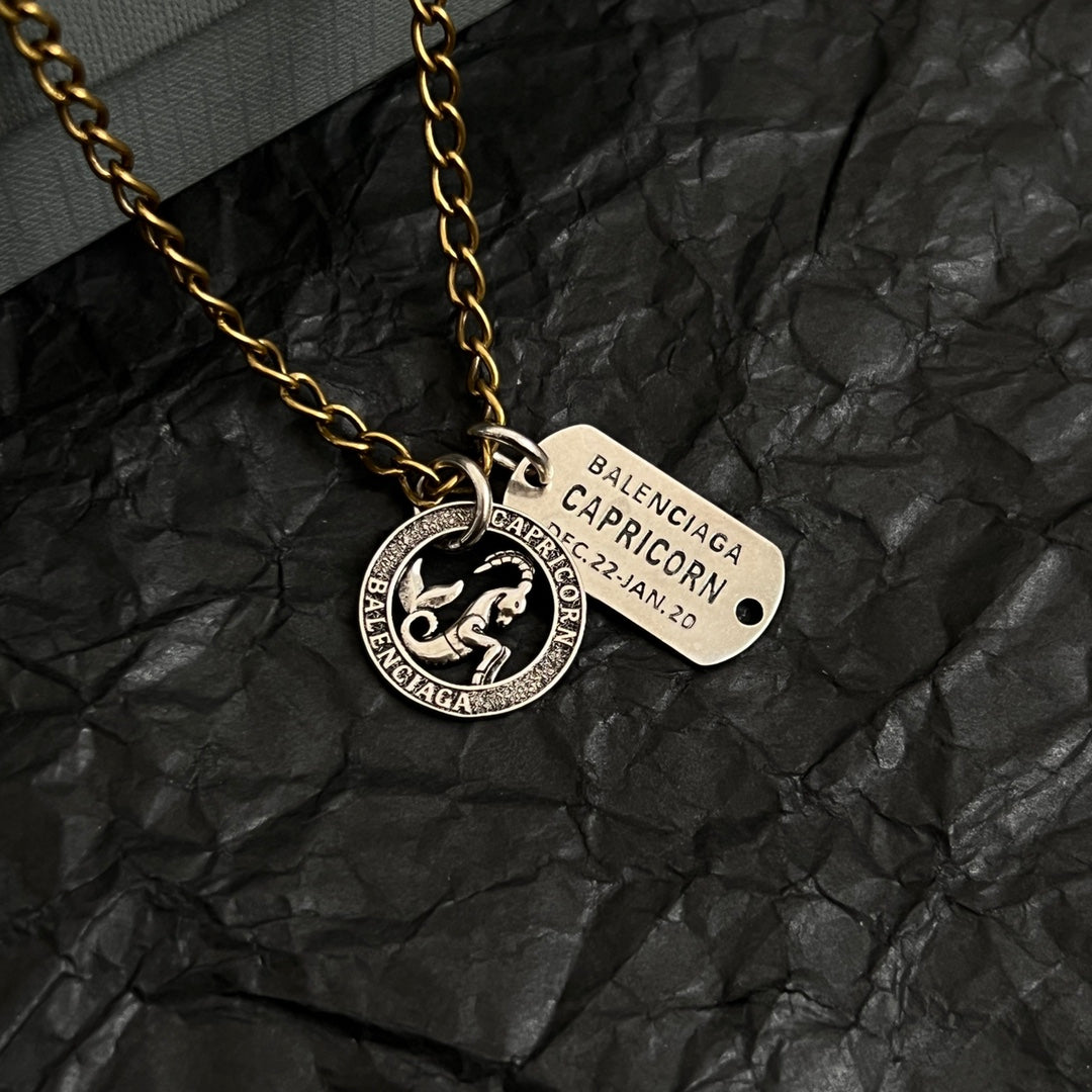 Gold charm necklace with circular zodiac coin and beige engraved name tag