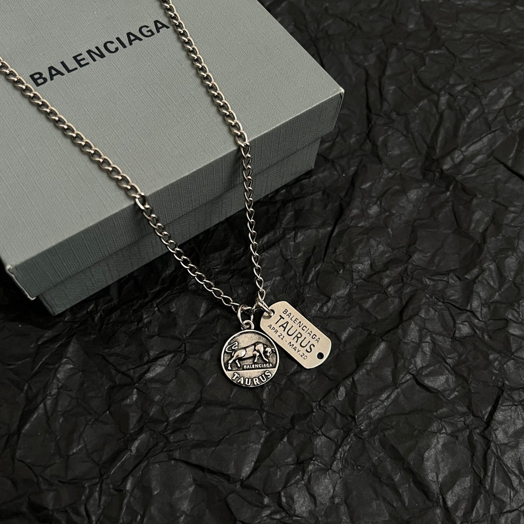 Balenciaga charm necklace with two pendants, silver chain lying on gray box