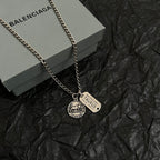 Balenciaga charm necklace with two pendants, silver chain lying on gray box