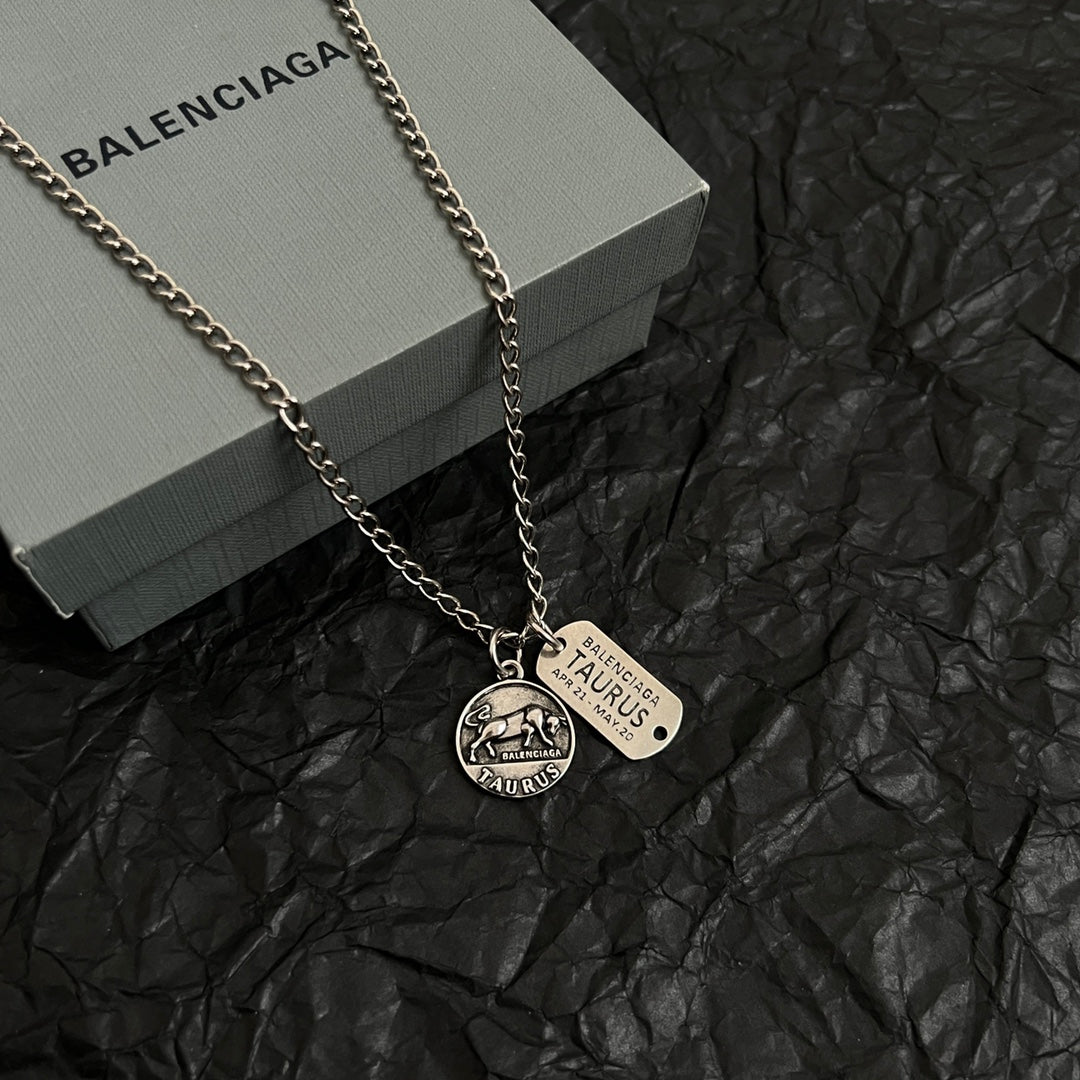 Balenciaga charm necklace with two pendants, silver chain lying on gray box