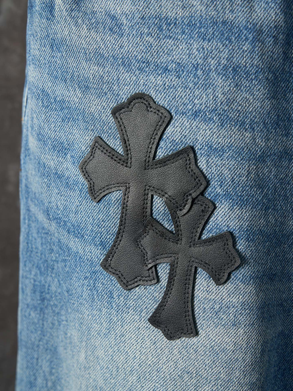 Light blue denim pants with a large black cross patch on the leg