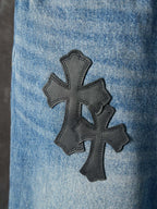 Light blue denim pants with a large black cross patch on the leg