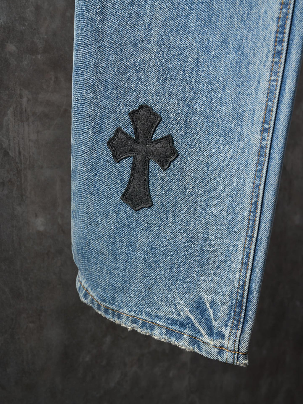 Light blue denim pants close-up: black cross patch on hem area