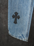 Light blue denim pants close-up: black cross patch on hem area
