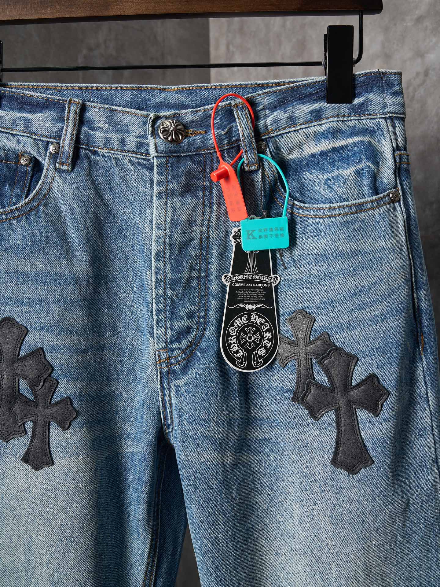 Light blue denim pants close-up: button fly and black cross patches