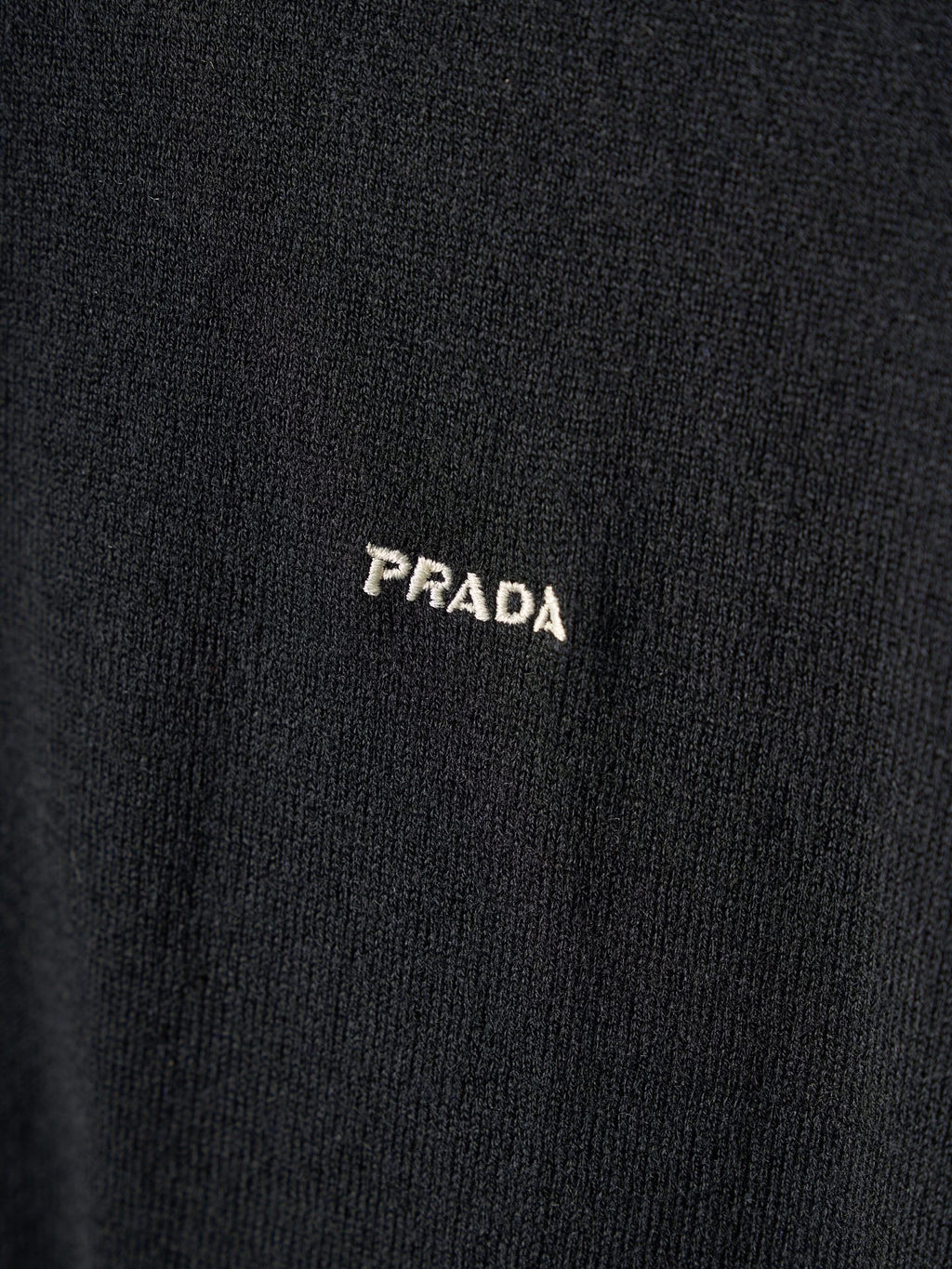 Close-up of PRADA embroidered logo on black knit sweater