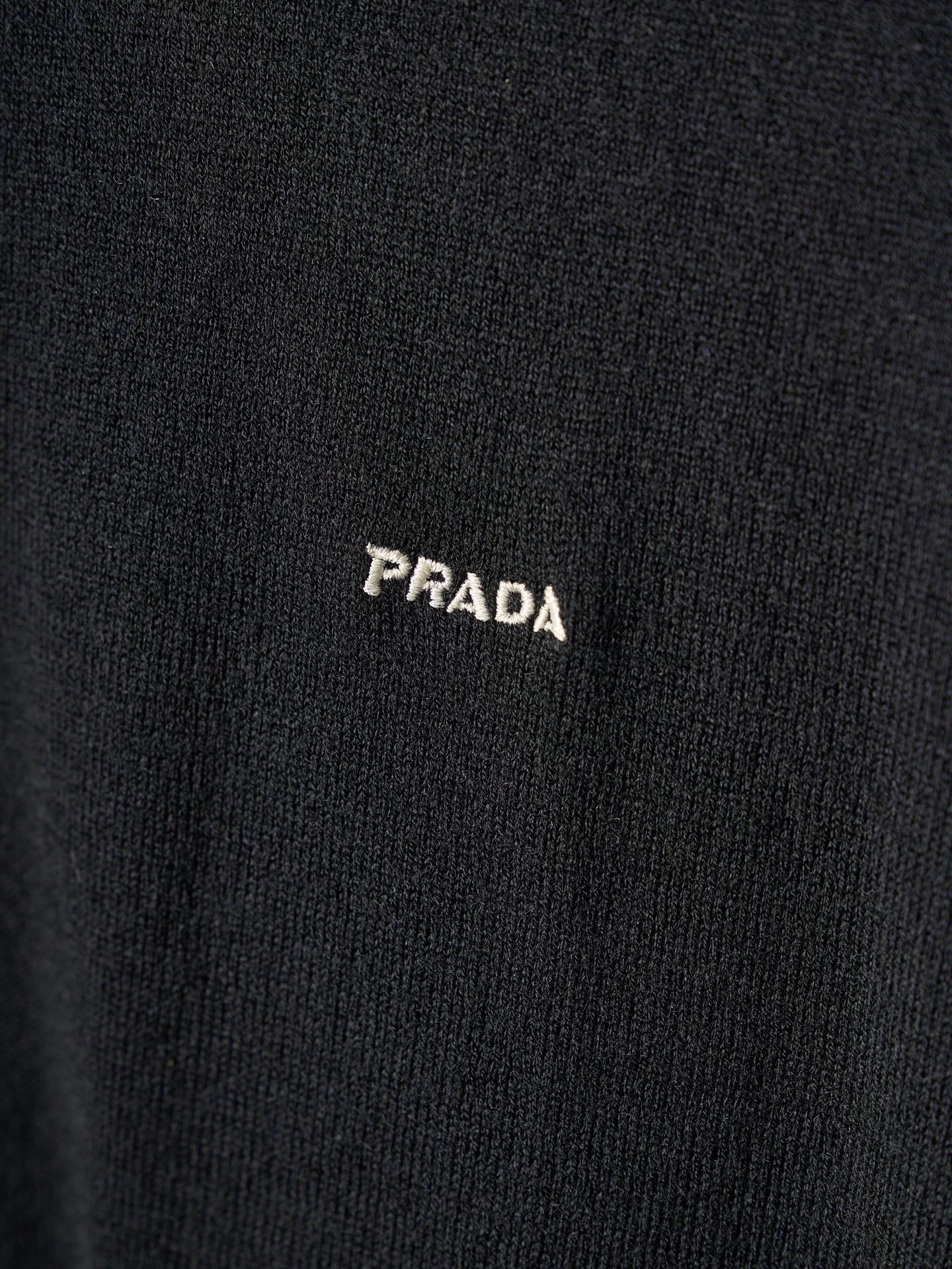 Close-up of PRADA embroidered logo on black knit sweater
