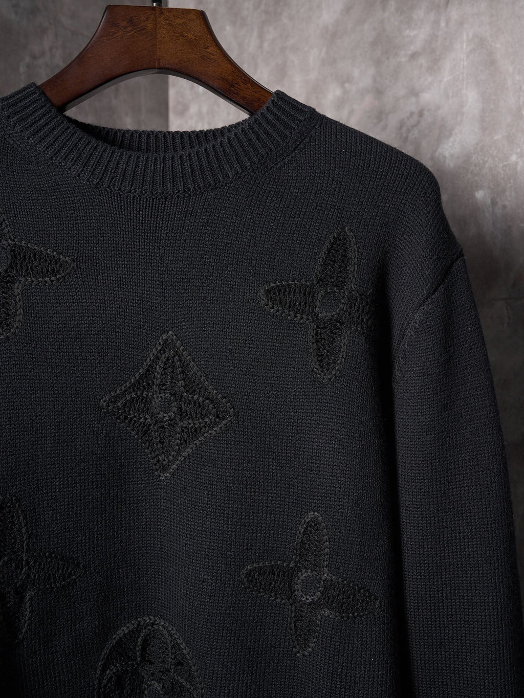 Black knit sweater close-up with embroidered monogram motifs and ribbed collar