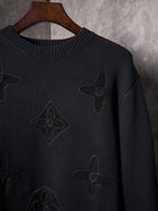 Black knit sweater close-up with embroidered monogram motifs and ribbed collar