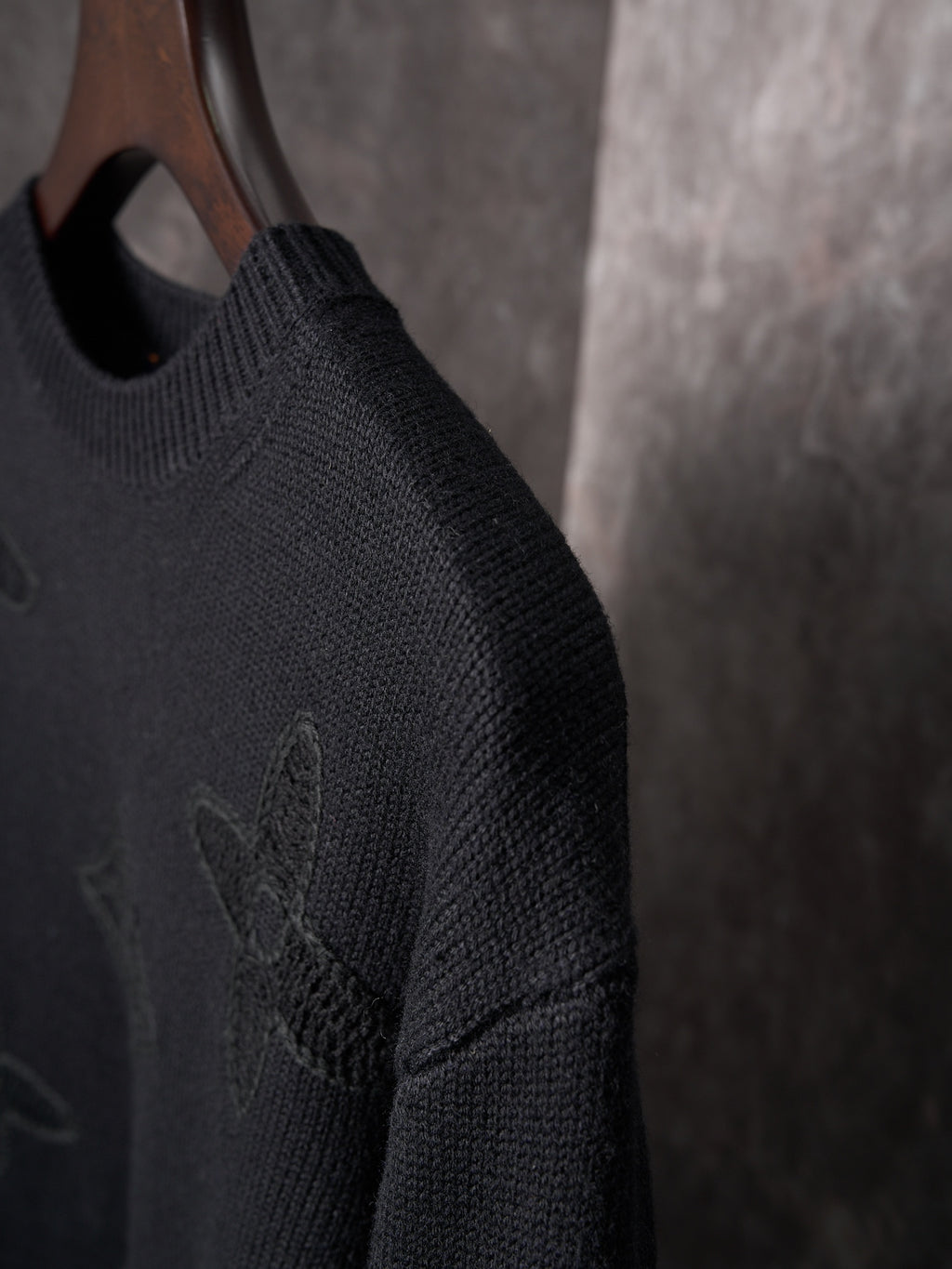 Black knit sweater side view with embossed monogram motif on sleeve