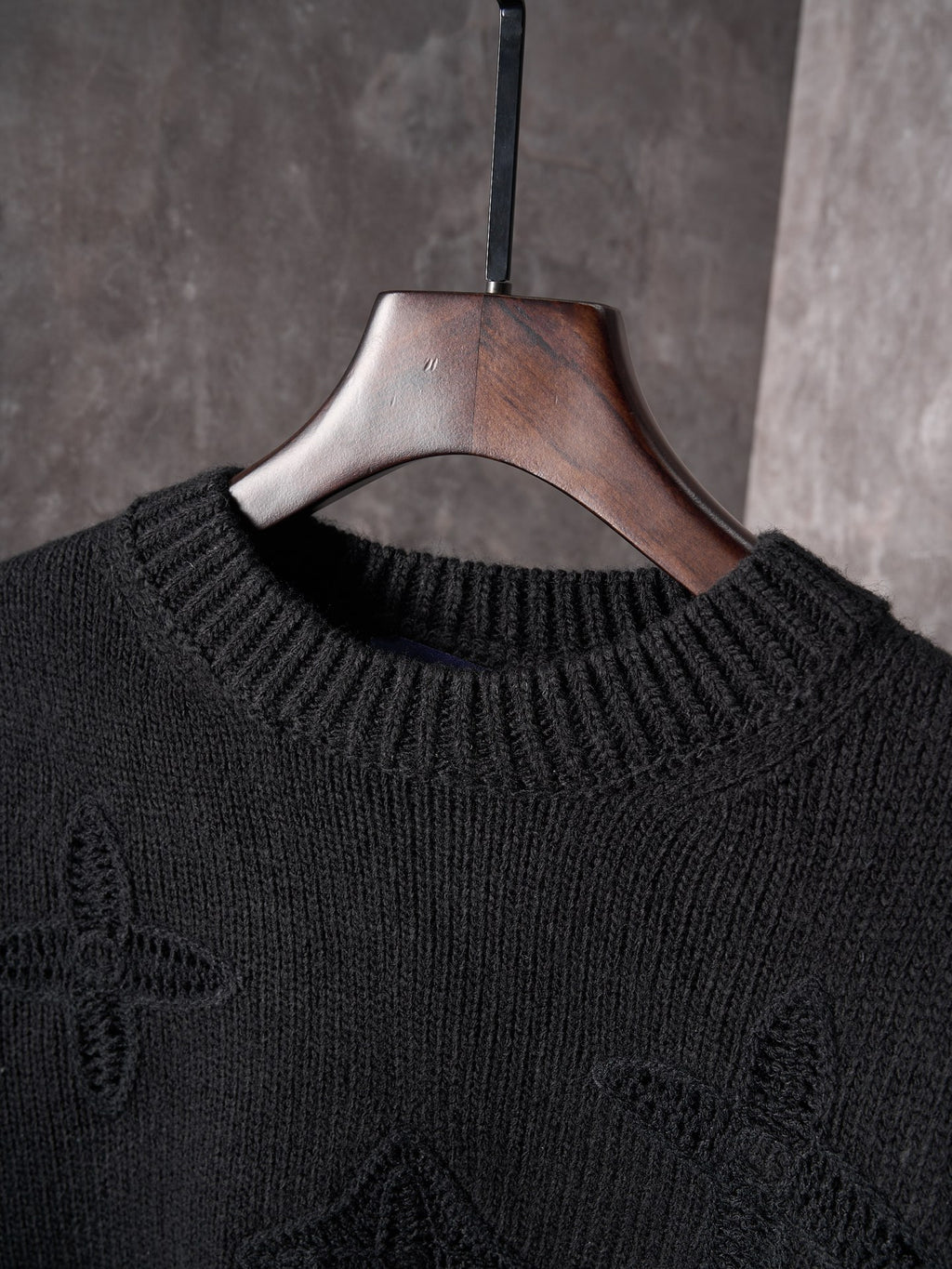 Black knit crewneck sweater neckline and ribbed collar on wooden hanger