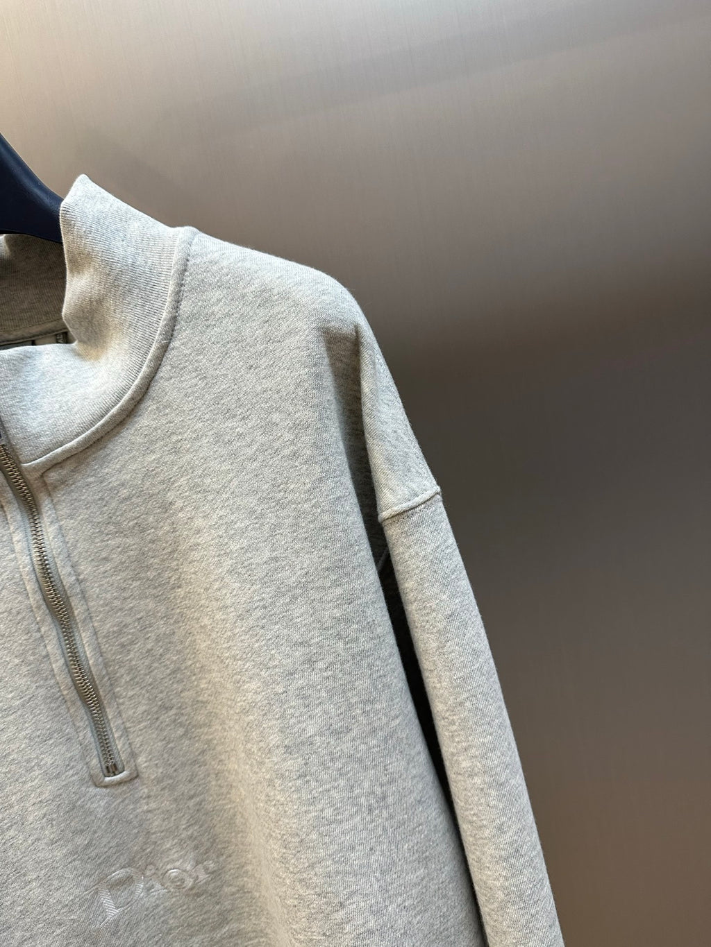 Light gray half-zip sweatshirt detail with vertical zipper and ribbed neck opening