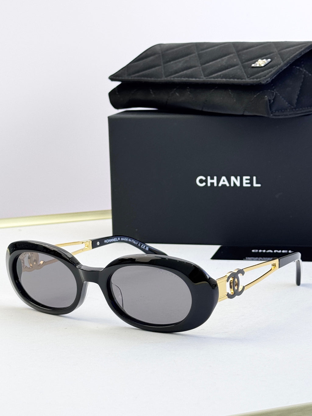 Designer round glasses, black frame with gold logo detail, clear lenses