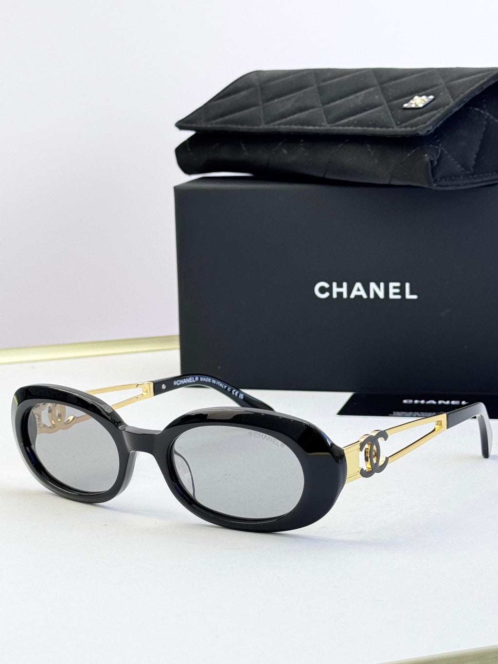 Designer round glasses, black frame with gold logo detail, tinted dark lenses