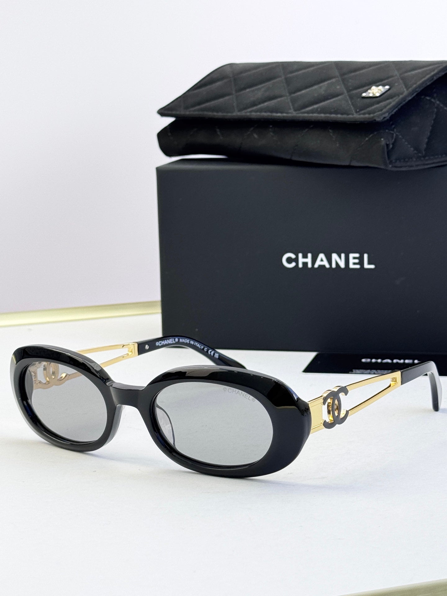 Designer round glasses, black frame with gold logo detail, tinted dark lenses