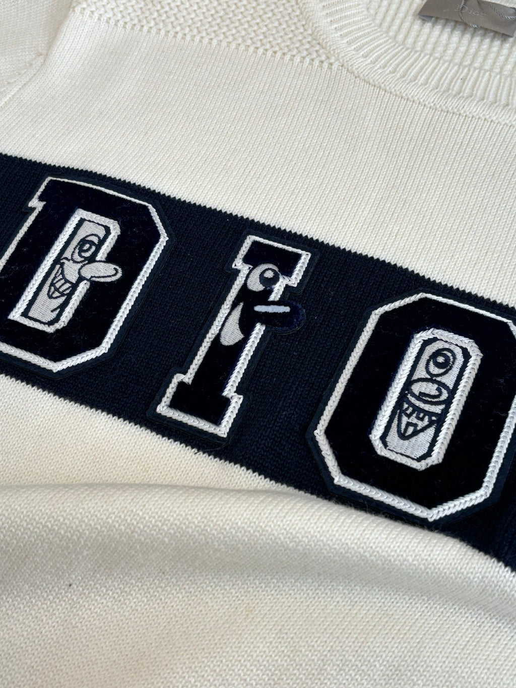 Dior sweater chest graphic with outlined letters on dark band, cream base