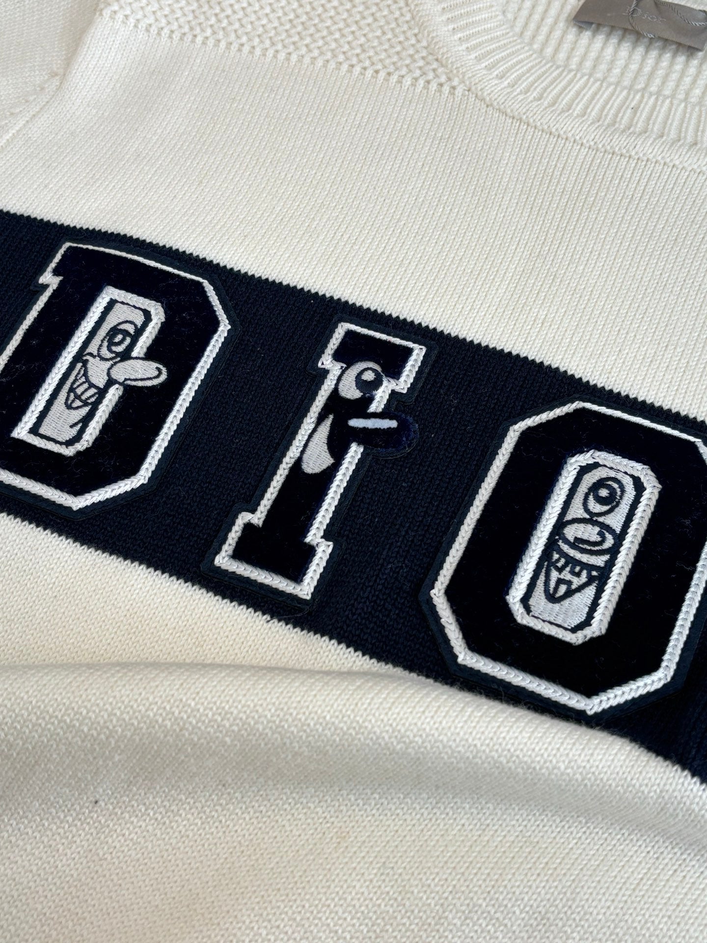 Dior sweater chest graphic with outlined letters on dark band, cream base