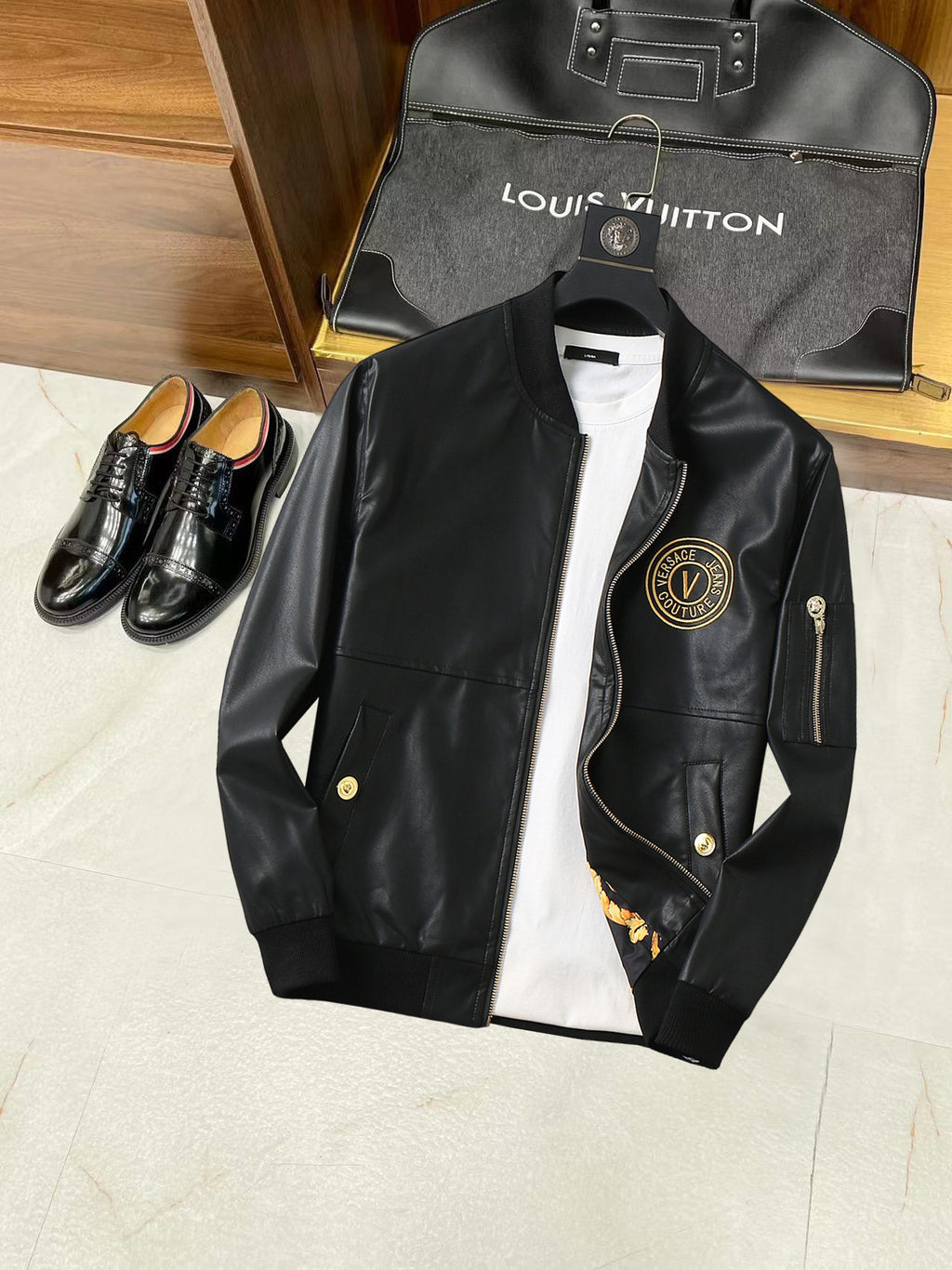 Black leather jacket with front zipper and gold logo patch detail over a white shirt
