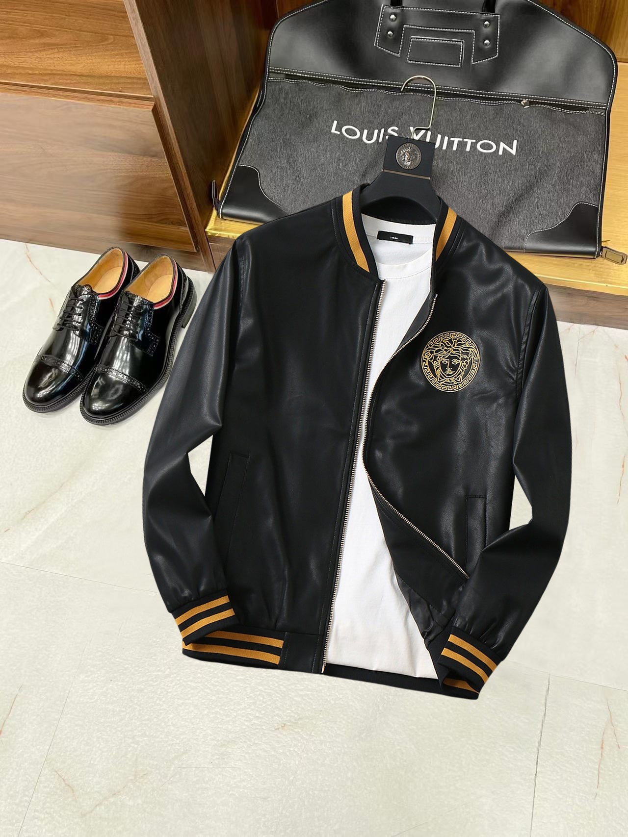 Black leather bomber jacket with gold medallion logo on the chest and zip front