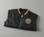 Black leather bomber jacket, flat lay, with gold medallion logo and ribbed trim collar