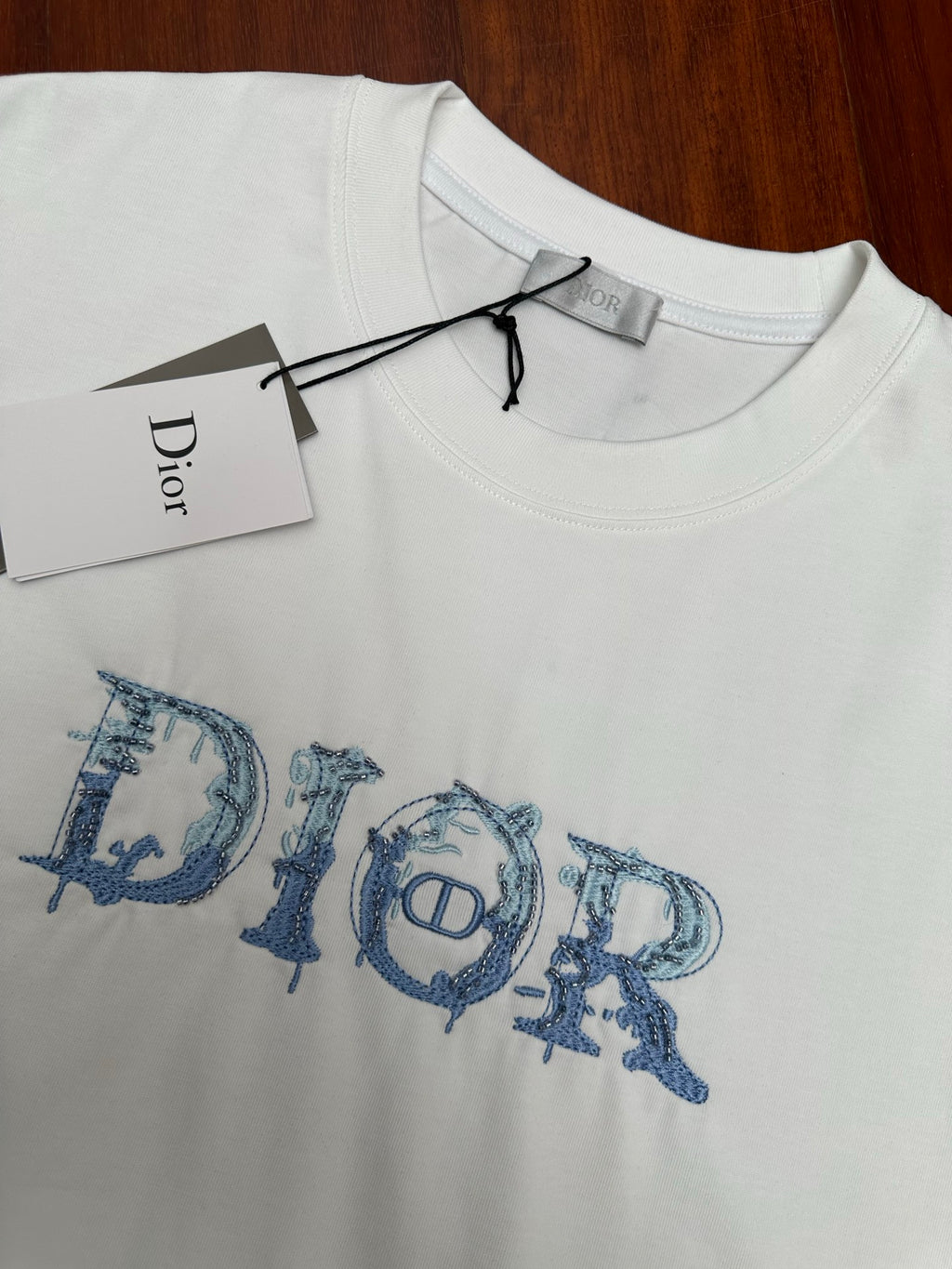 White crewneck T-shirt with blue Dior logo graphic and hanging label