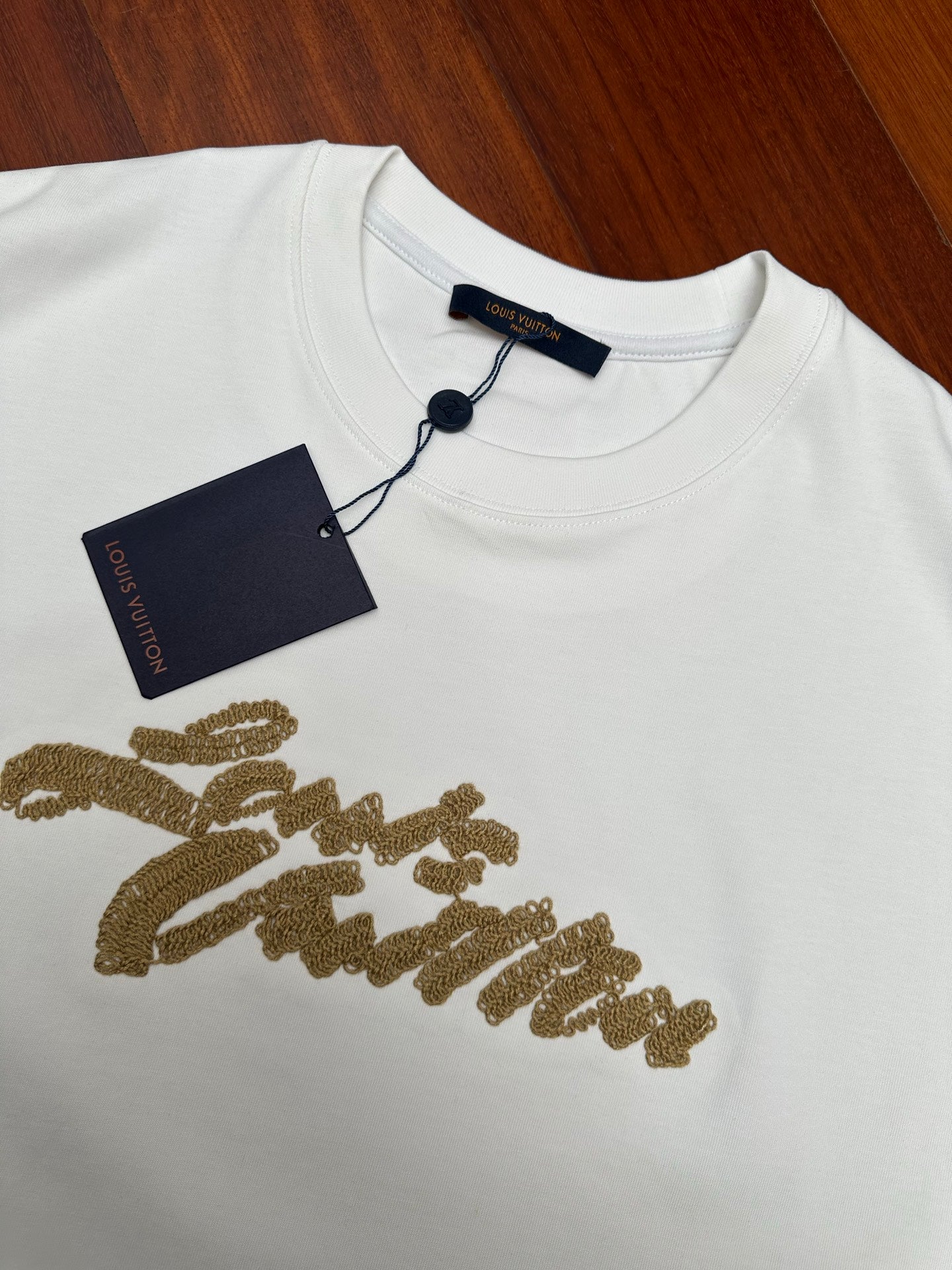 Louis Vuitton white short-sleeve shirt with gold embroidered script and navy hang tag