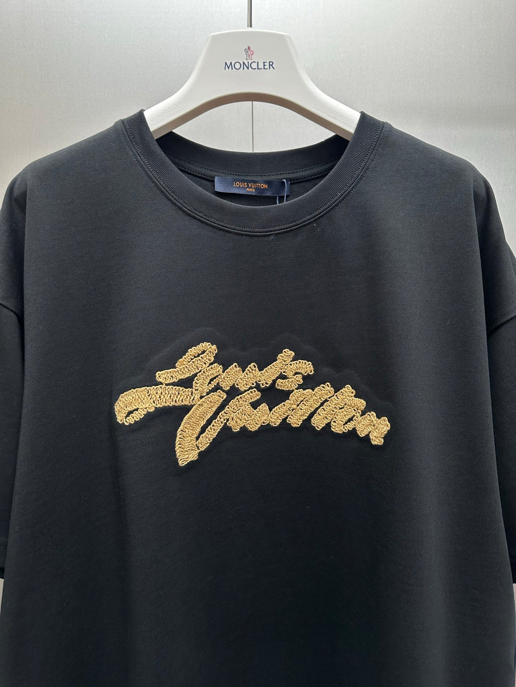 Louis Vuitton black crewneck T-shirt with gold embroidered script logo, chest close-up