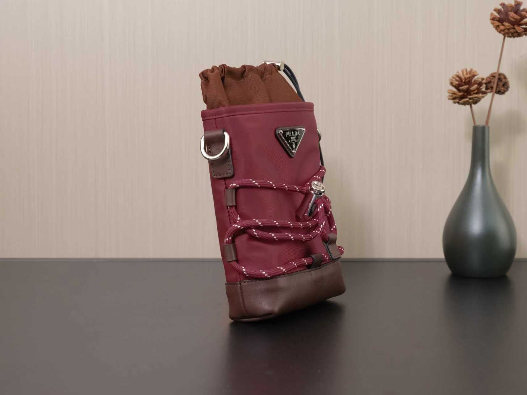Burgundy mini bucket bag with gathered top, side hardware, and brown trim