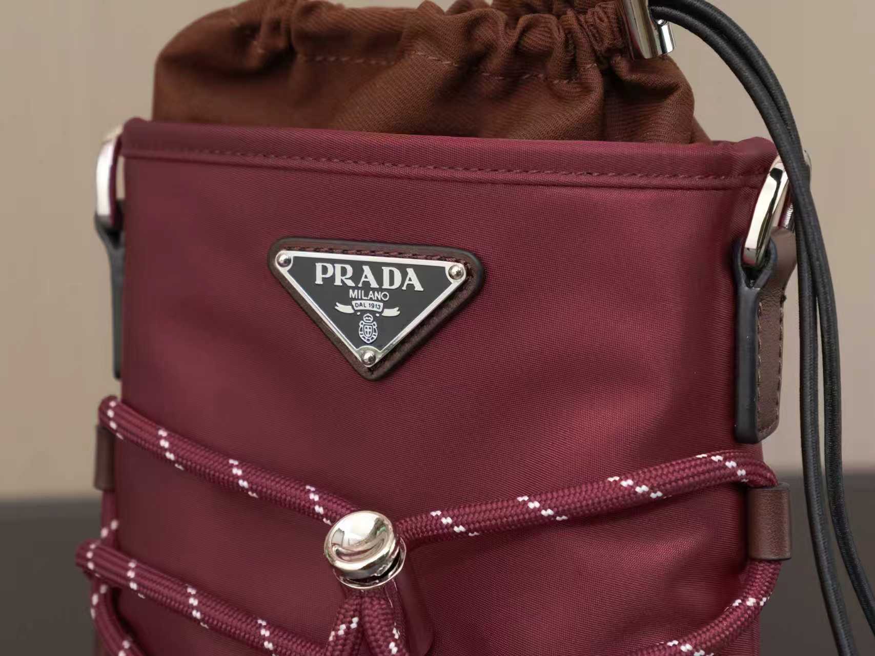 Burgundy Prada bag front with triangular logo plate, drawstring and metal rings
