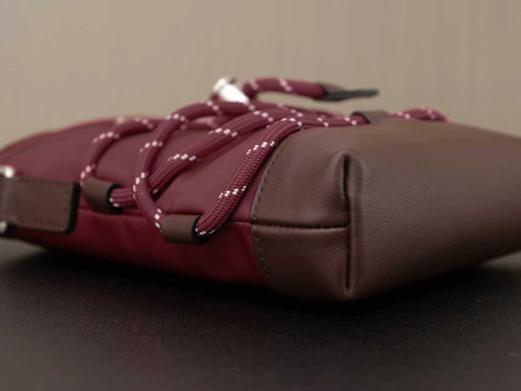Burgundy bag with brown leather base, braided drawstring ties, and silver hardware