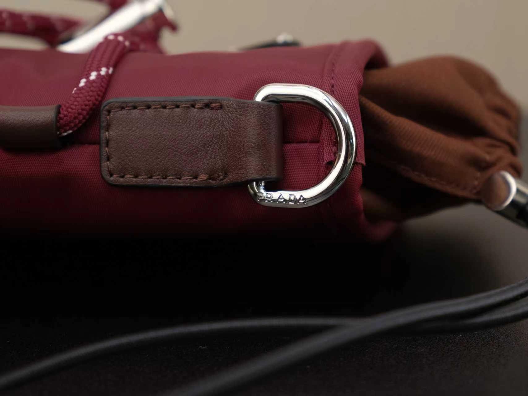 Brown leather strap tab with oval buckle and silver hardware on burgundy bag