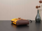 Prada bag with yellow body and brown side pocket, lying on its side.