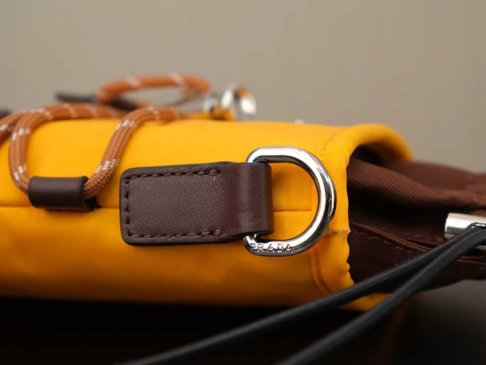 Yellow Prada bag close-up with brown D-ring strap and textured trim.
