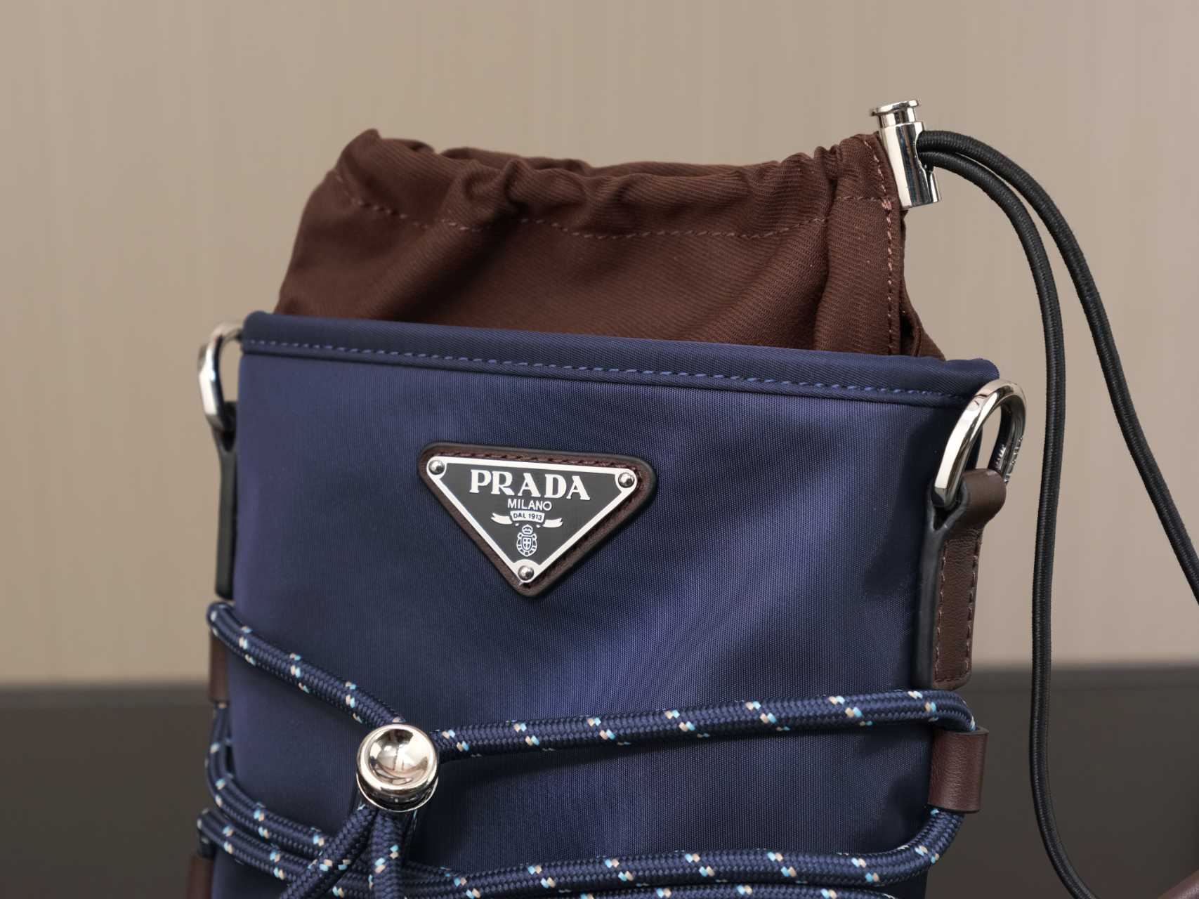 Prada shoulder bag front view with dark blue flap, brown top drawstring, and logo plaque