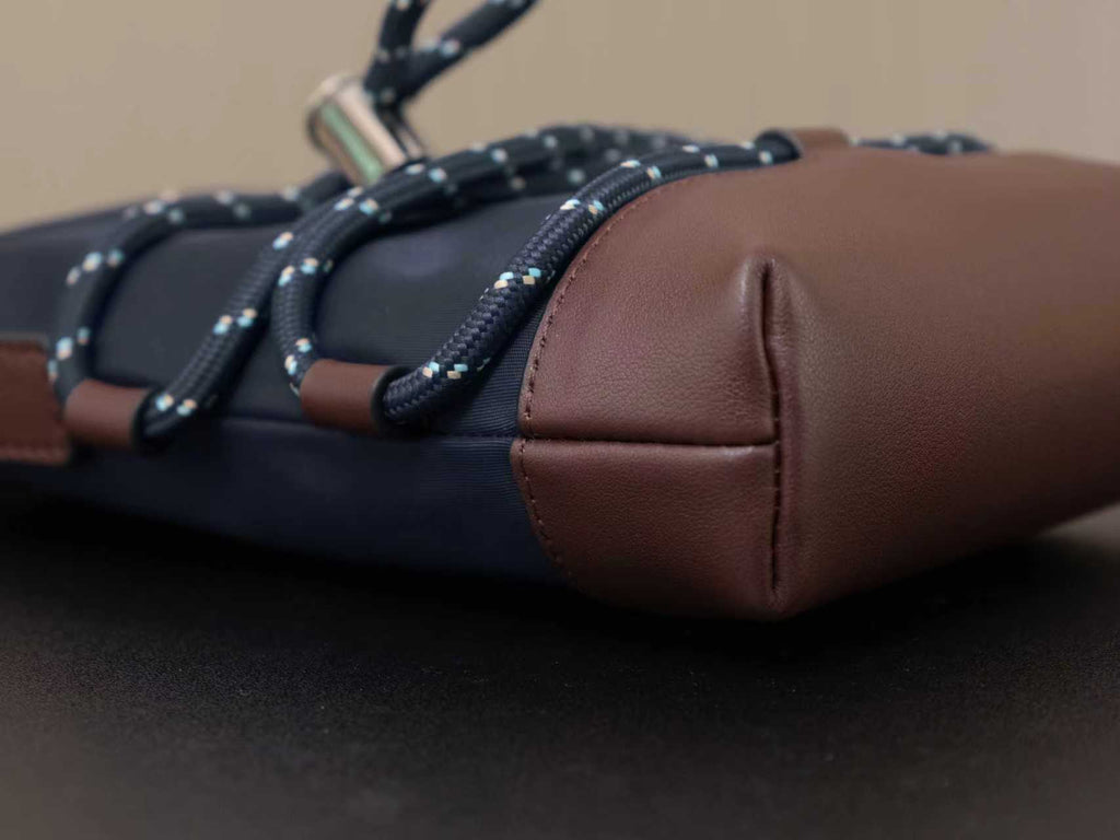 Prada bag side close-up with dark blue fabric, brown end panel, and braided strap trim