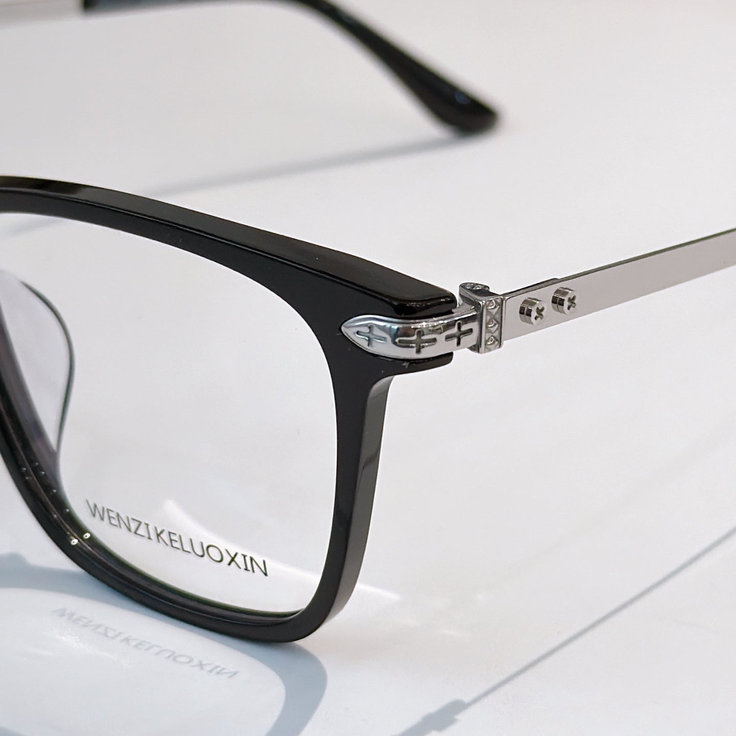 Black eyeglass frame with metal hinge detail and clear lenses.