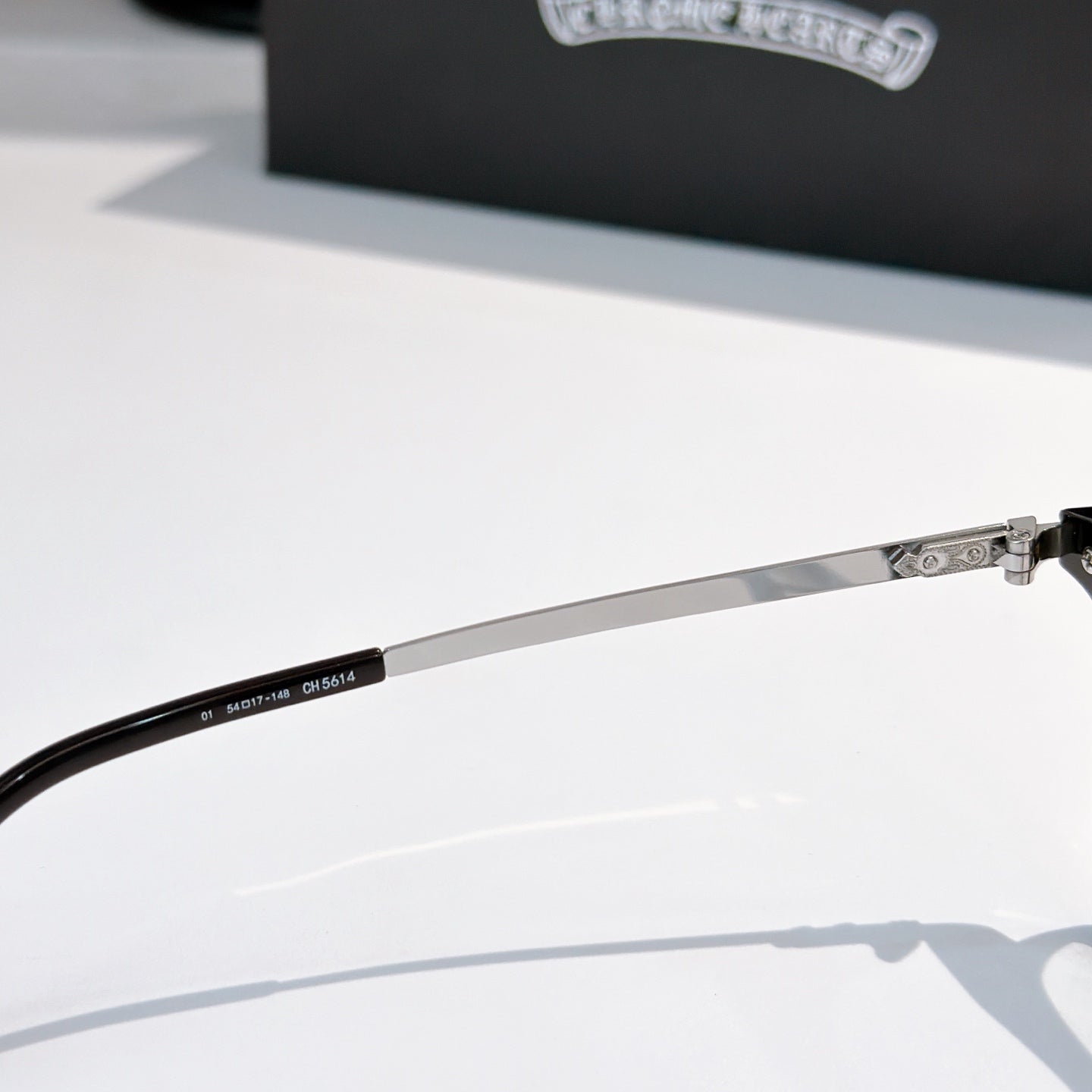 Metal eyeglass arm with markings and clear lens frame, side view.