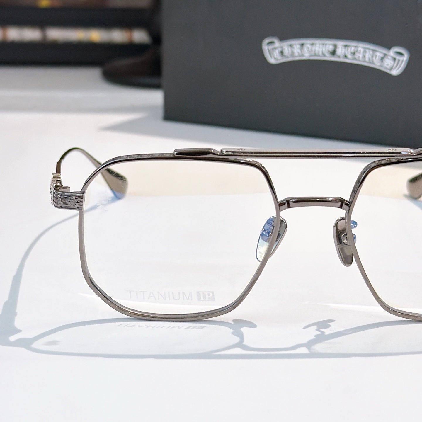 Metal eyeglass frame with clear lenses, embossed temple arms and bridge detail.