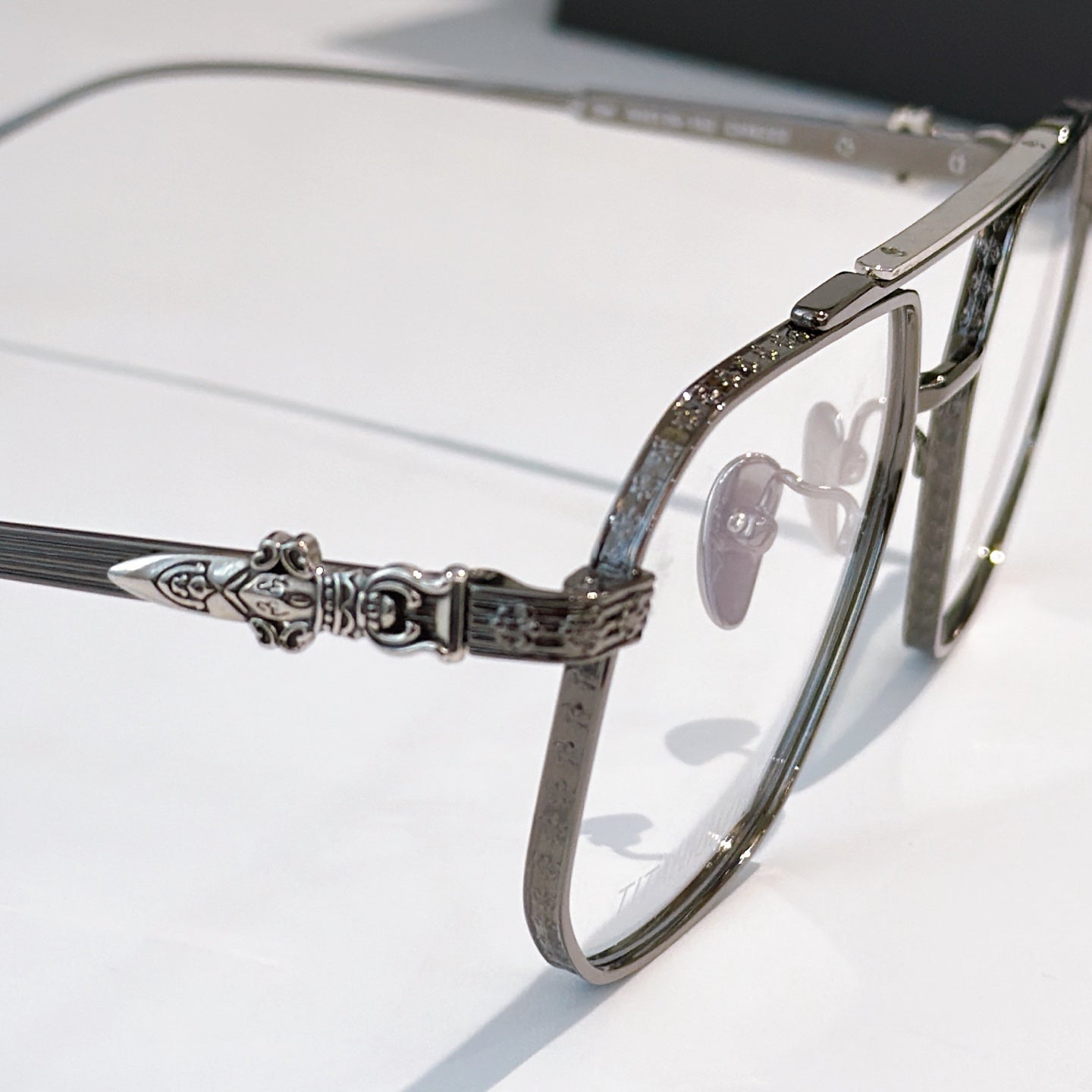 Ornate metal eyeglasses temple with decorative hinge and clear lenses.