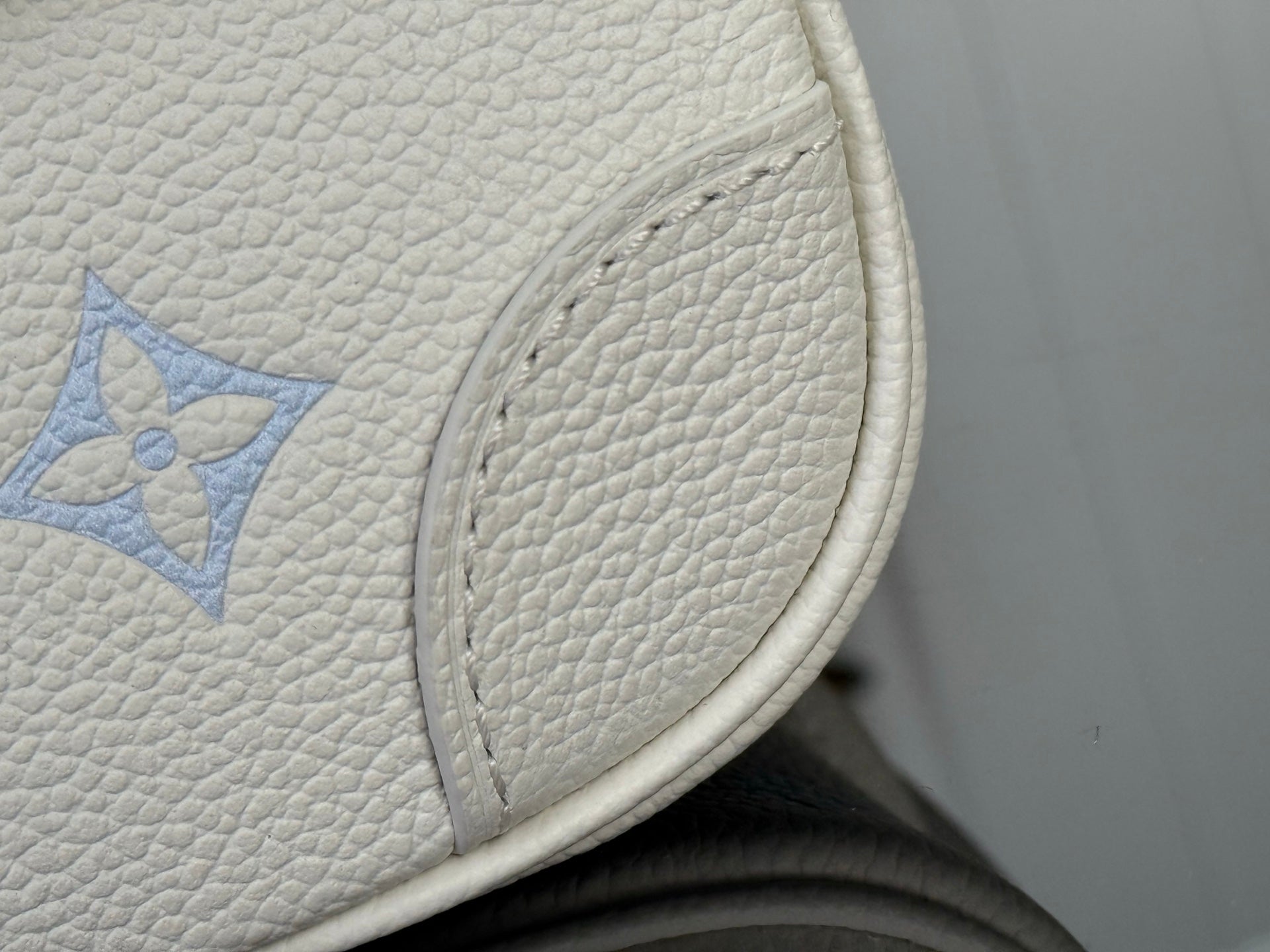 Louis Vuitton monogram leather edge detail on white bag, blue pattern