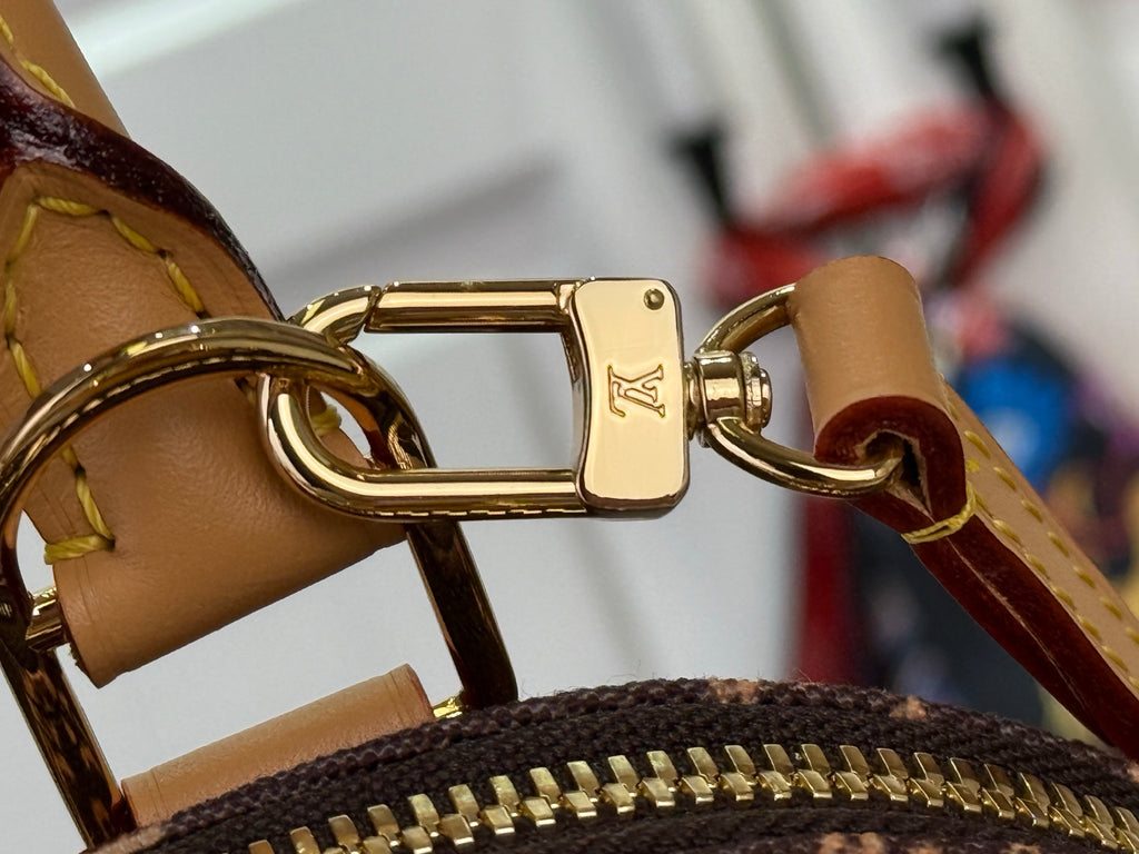Tan leather strap with gold-tone buckle and clasp attached to monogram canvas