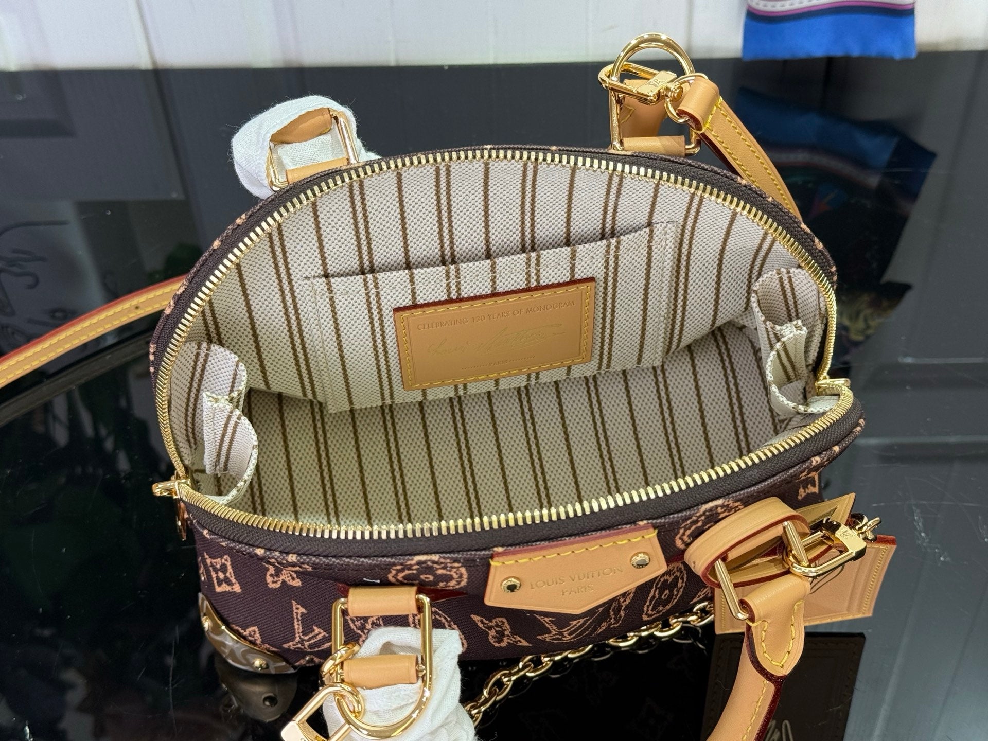 Open monogram handbag showing striped fabric lining and tan leather interior pocket