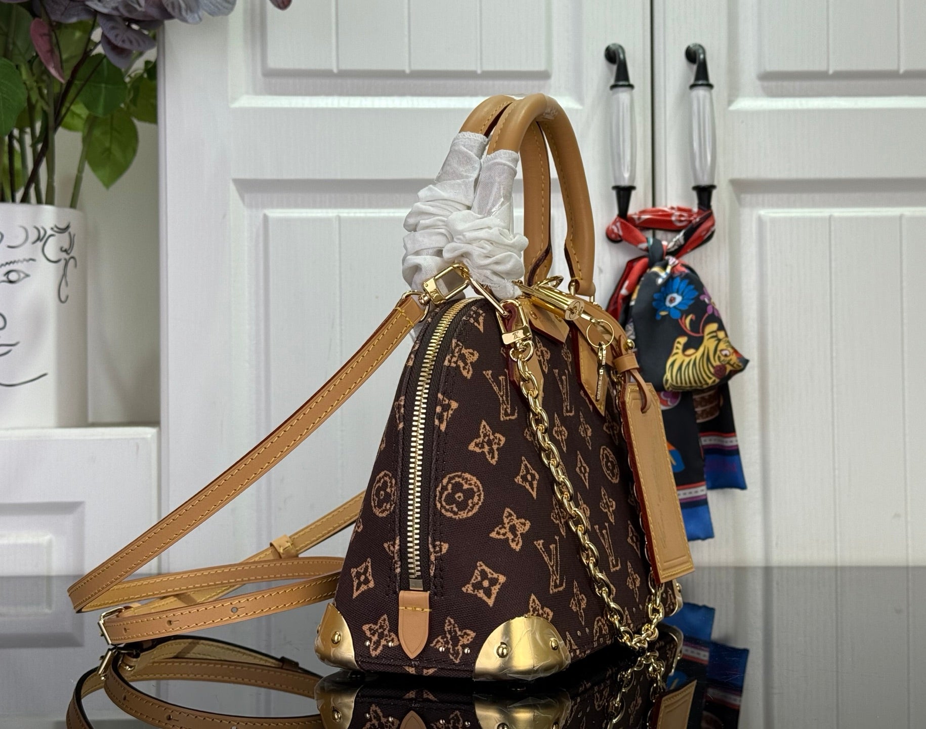 Monogram handbag with top handle, tan leather strap, gold zipper hardware and side pocket