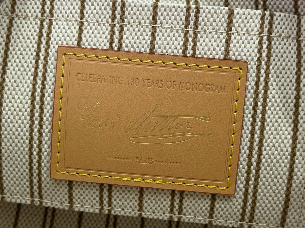 Tan leather label reading “CELEBRATING 130 YEARS OF MONOGRAM” on striped fabric