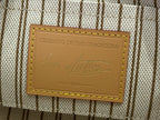 Tan leather label reading “CELEBRATING 130 YEARS OF MONOGRAM” on striped fabric