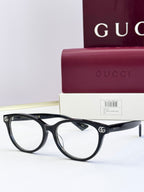 Black eyeglass frames with clear lenses and gold logo detail at temples