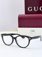 Black eyeglass frames with clear lenses and gold logo detail at temples